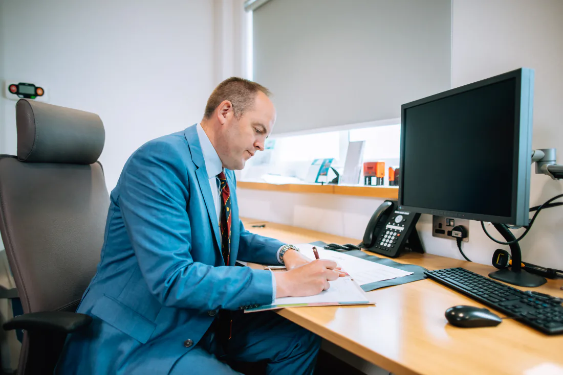 Mr West at his desk in clinic, writing up notes.