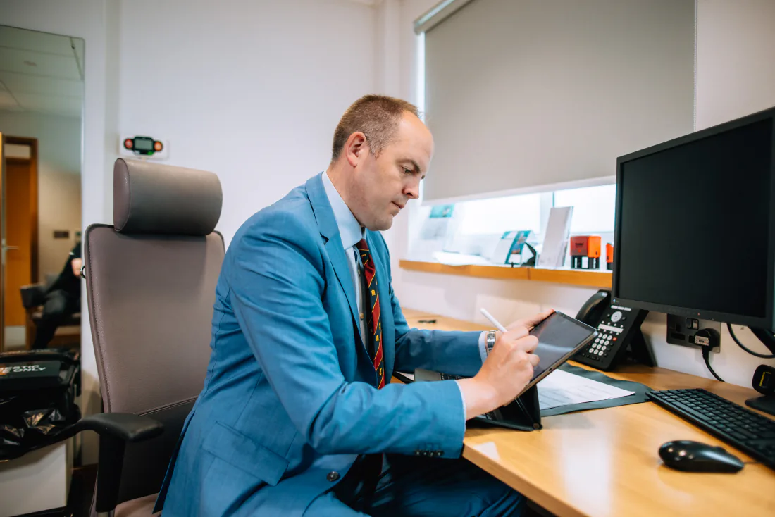 Mr West at his desk in clinic, reading results on a tablet.