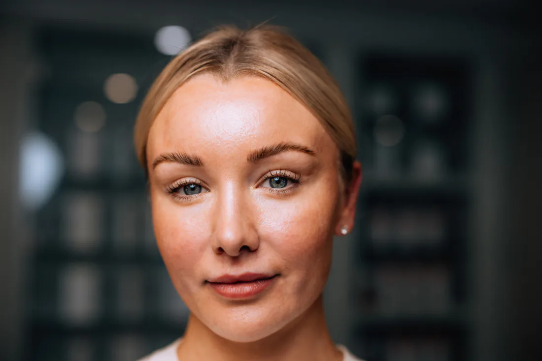 A woman with fair hair tied back looking at the camera against a dark background.