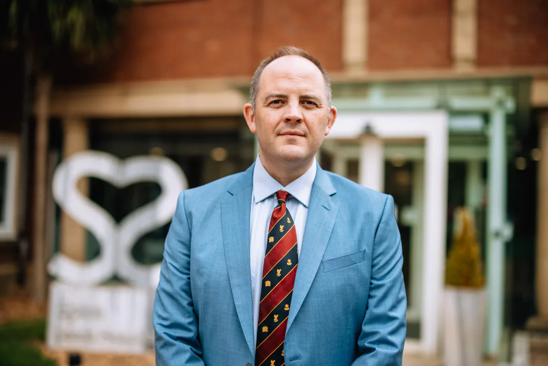 Mr Christopher West in a blue suit outside Spire Leeds Hospital, the hospital sign behind him.