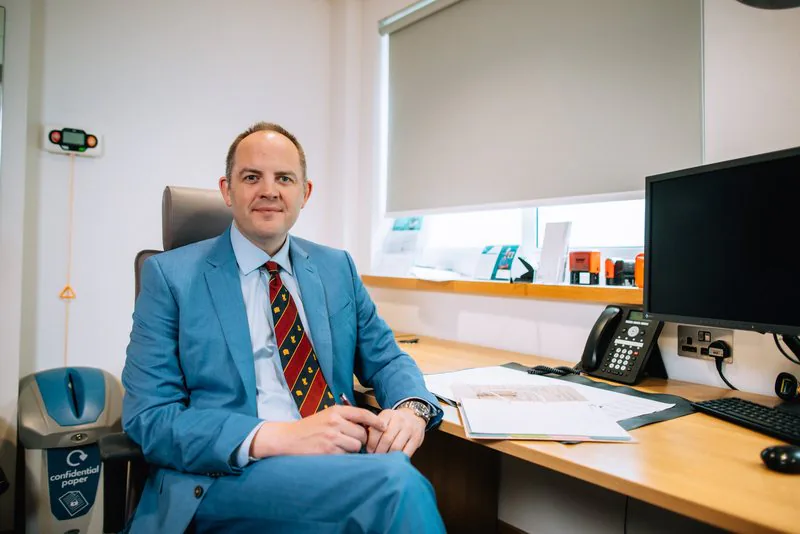 Mr Christopher West in a blue suit at his consulting room desk.