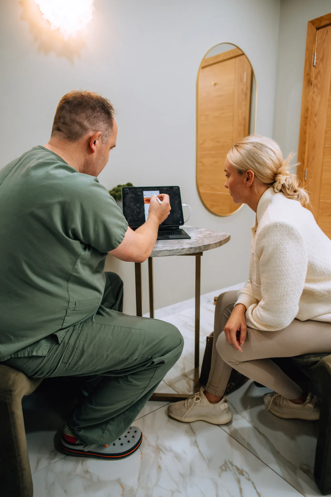 Mr Christopher West in green scrubs showing a woman a tablet screen.