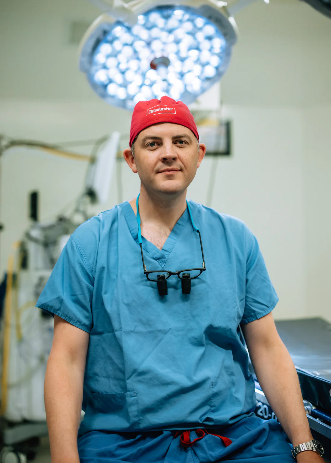 Mr Christopher West in blue scrubs and a red theatre cap in an operating theatre.