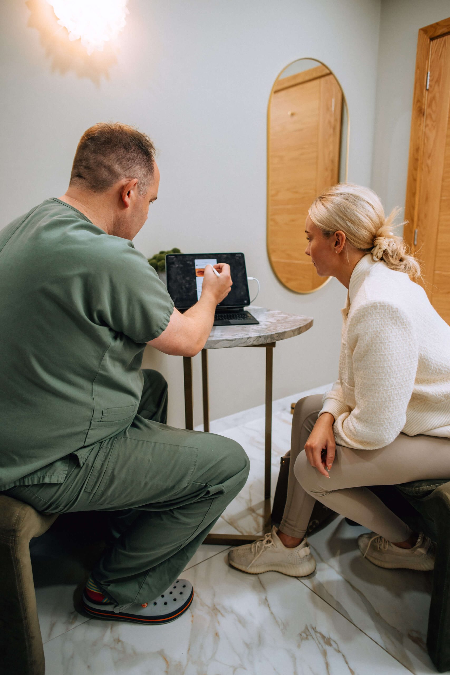 Mr West in green scrubs showing a woman a tablet screen