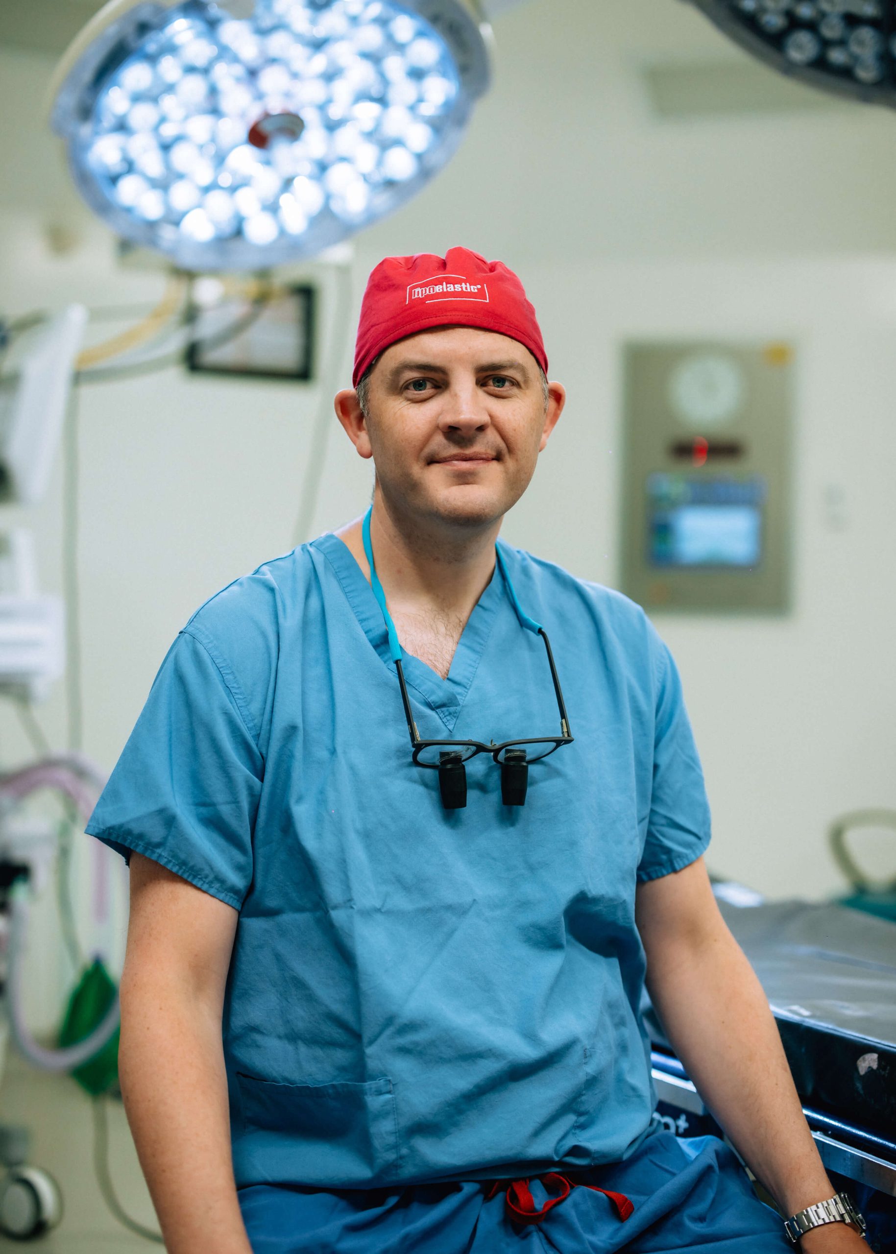 Mr West in blue scrubs and a red theatre cap in an operating theatre